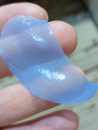 Close-up of a translucent blue under-eye patch held between fingers, showing its glossy texture.