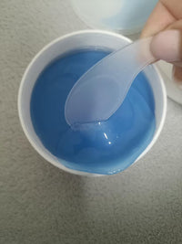 Hand holding a translucent under-eye patch above an open jar of blue gel patches