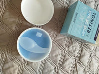 Open jar of blue under-eye patches with a spatula, white lid and Xioimy box on lace fabric