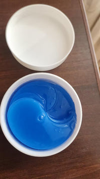 Open white jar filled with blue under-eye patches, with its lid behind it on a wooden surface.