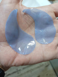 Two translucent blue crescent-shaped under-eye patches resting in an open palm.