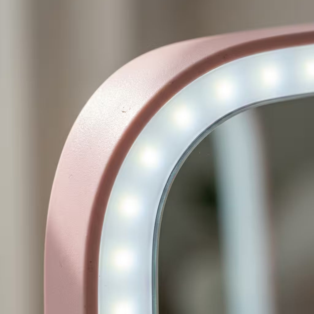 Close-up of a rounded rectangular LED vanity mirror with a matte blush pink frame and glowing white light around a reflective mirror surface.