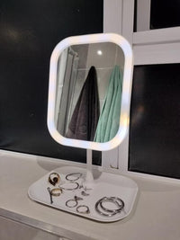 Lighted makeup mirror with jewelry on a stand against a black background